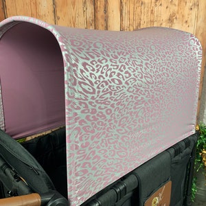 May include: A pink and silver leopard print canopy for a stroller or wagon. The canopy is made of a soft, breathable fabric and provides shade and privacy for a child.