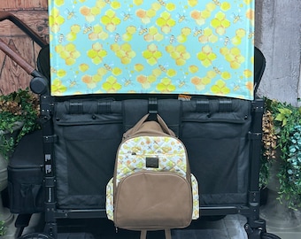 May include: A black double stroller with a blue and yellow honeycomb patterned canopy. A brown backpack with a white and yellow pattern is hanging from the stroller.