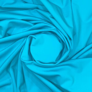 May include: A close-up of a bright turquoise fabric, with soft folds and wrinkles, creating a circular pattern in the center.