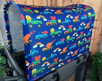 May include: A blue stroller canopy with a colorful pattern of smiling faces, hearts, rainbows, and trucks. The canopy is made of a lightweight, breathable fabric and is designed to protect your child from the sun and wind.