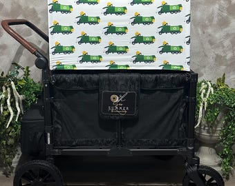May include: A black utility wagon with a white canopy featuring a repeating pattern of green recycling trucks. The wagon has black wheels, a brown handle, and a black storage compartment with a label that reads "Oh Summer".