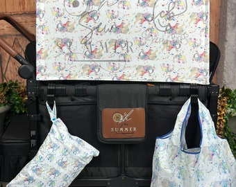 May include: A black stroller featuring a white canopy with a colorful elephant and paint splatter print. The canopy displays the text Oh Sew SUMMER. A matching white elephant print storage bag and a tote bag hang from the stroller frame.