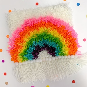 Könnte beinhalten: Ein regenbogenfarbener Garnteppich mit einem weißen Fransen. Der Teppich ist regenbogenförmig mit einer weißen Mitte.