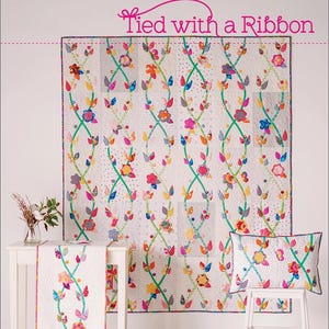 May include: A white quilt, table runner, and pillow set with a colorful floral trellis design. The set includes a large quilt, a table runner, and a pillow, all featuring a repeating pattern of flowers and leaves. The text "Tied with a Ribbon" is at the top.