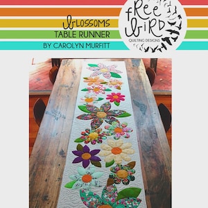 May include: A floral table runner with large, colorful flower appliqués in shades of pink, orange, yellow, and purple. The runner is on a wooden table. Text on the image reads "Blossoms Table Runner by Carolyn Murfitt" and "Free Bird Quilting Designs."