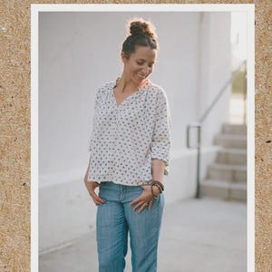 May include: A woman wearing a white blouse with a small black dot pattern and blue jeans. The image is framed with a white border and set against a textured brown background. The text "SEW LIBERATED" and "MATCHA TOP" are also visible.