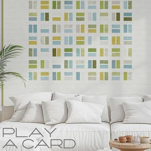 May include: A large framed artwork with a geometric pattern in shades of green, blue, and yellow. The artwork hangs above a white sofa with several white pillows. The text "PLAY A CARD" and "ZEN CHIC" are visible.