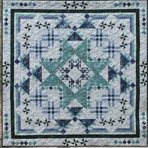 May include: A square quilt with a geometric design in shades of teal, blue, and white. The quilt features a central starburst pattern and is bordered by a dark teal frame. The word "Crossroads" is at the top, and "Whirligig Designs" is at the bottom.