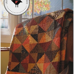May include: A patchwork quilt in autumnal colors, featuring triangles of orange, brown, and rust fabrics. The quilt measures 52" x 64". The image includes a logo with the text "Laugh Yourself Into Stitches".