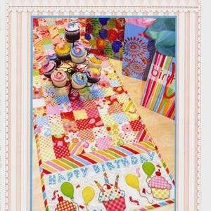 May include: A colorful Happy Birthday table runner with a patchwork design. The runner features cupcakes, balloons, and the words "Happy Birthday." The image also includes a cupcake stand with cupcakes and gift bags.
