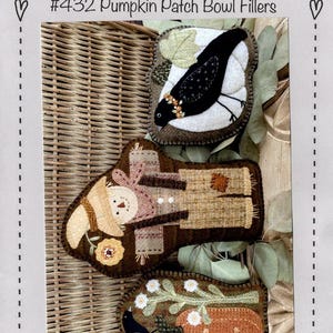 May include: Three wool bowl filler designs with a pumpkin patch theme. The designs include a black bird, a scarecrow, and a pumpkin with a bird. The bowl fillers are approximately 4 to 6 inches wide and 5 to 8 inches high. The text "Heart to Hand" is also visible.