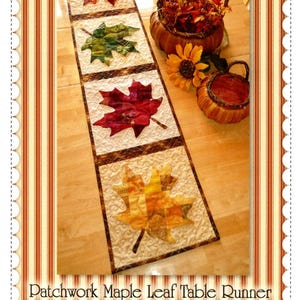 May include: A patchwork maple leaf table runner with four colorful leaf designs. The runner is on a light wood surface, with a basket of fall foliage and a sunflower nearby. The text "Shabby Fabrics" and "Patchwork Maple Leaf Table Runner" are visible.