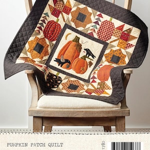 May include: A quilted pumpkin patch quilt, size 30" x 30", draped over a wooden chair. The quilt features orange pumpkins, fall foliage, and a black border. The quilt is made by Buttermilk Basin Design Co.
