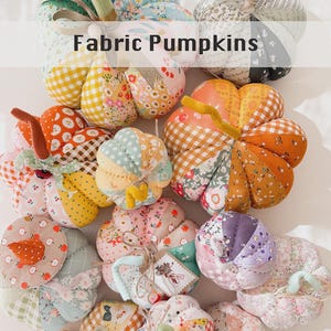 May include: A collection of handmade fabric pumpkins in various sizes, featuring patchwork designs with floral, gingham, and polka dot patterns in orange, pink, blue, and green. Each pumpkin has a fabric stem and some include twine tags.