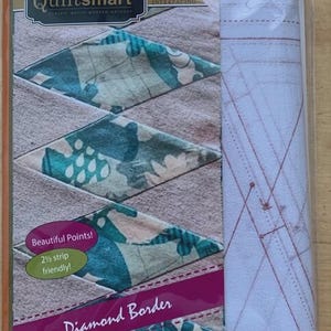 May include: A package of quilting supplies featuring a diamond border design. The package includes printed interfacing and fabric with a teal and beige pattern. Text on the package reads "Quiltsmart" and "fast-easy-smart!"