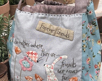May include: A blue and white fabric tote bag with a floral pattern and the text "Forever Friends" and "No matter where they are... friends are never far". The bag has a brown fabric handle and a white bunny with a pink flower.