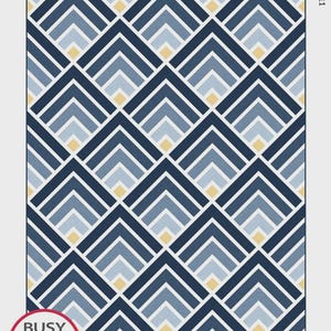 May include: A quilt pattern titled "Mountain Peaks" featuring a geometric design of navy blue, light blue, and yellow chevron shapes. The pattern is designed by Myra Barnes and includes four sizes. The Busy Hands Quilts logo is visible.