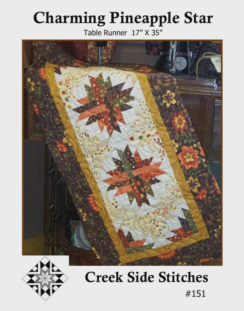 K&ouml;nnte beinhalten: Gesteppter Tischl&auml;ufer mit Sternmuster in herbstlichen Farben wie Orange, Gr&uuml;n und Braun. Der L&auml;ufer ist 43 cm x 89 cm gro&szlig;, mit dem Text "Charming Pineapple Star" und "Creek Side Stitches".
