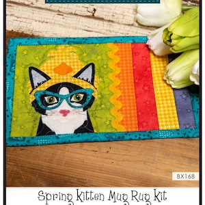 May include: A spring kitten mug rug kit with a black and white cat wearing glasses and a yellow hat. The mug rug is made with colorful fabrics and has a rainbow design. The kit includes instructions, precut fused appliqué, and all of the fabric to complete the mug rug. Finished size: 10" x 6".