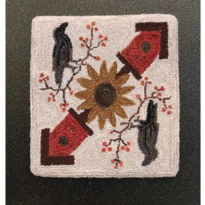May include: A square, off-white rug with a central sunflower design, surrounded by two red birdhouses and two black birds. Branches with red berries are interspersed throughout. The text "Garden Gals August" is at the bottom.