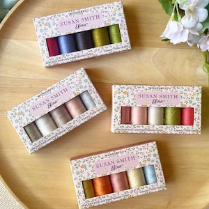 May include: Four boxes of Susan Smith Efina thread spools in various colors, including red, blue, green, and neutral tones. The boxes have a floral design and contain five spools each. The thread is 100% extra long staple Egyptian cotton.