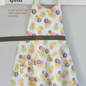 May include: Farmhouse apron with a white background and a colorful floral pattern in shades of orange, green, and gray. The apron has a dark gray neck strap and waist tie. The text "Farmhouse Apron" is visible.