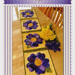 May include: A patchwork table runner featuring four large pansy flower designs. Each flower has purple petals and a yellow center, set against a yellow background. The text "Shabby Fabrics" and "Patchwork Pansy Table Runner" are visible.