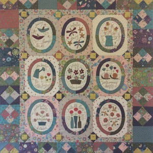 May include: A quilt with a patchwork design featuring nine oval-shaped panels with embroidered images and text. The panels are surrounded by a border of smaller squares with different patterns. The quilt is made in a variety of colors, including pink, blue, green, and brown. The text on the panels includes phrases like "See beauty in the little things" and "Bees buzzing happily".