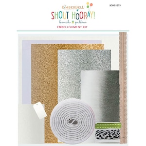 May include: Embellishment kit for a craft project. The kit includes gold and silver glitter paper, white paper, white ribbon, green ribbon, black and white twine, and a white tag. The kit is labeled "Shout Hooray! Bench & Pillow Embellishment Kit" and "KDKB1275".