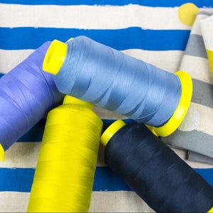 May include: Four spools of thread in blue, yellow, and black colors. The spools are arranged on a striped fabric background.