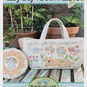 May include: A beige tote bag and round pillow with floral and cat designs. The tote bag has a handle and the text "lazy-day... gentle breeze... bird song... bliss...". The logo for "The Birdhouse Patchwork Designs" is at the bottom.