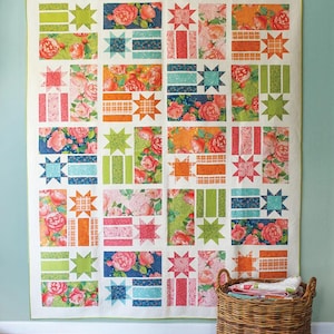 May include: A colorful quilt with floral and geometric patterns. The quilt features squares with roses, stars, and stripes in shades of pink, orange, green, and blue. The word "Constance" is at the top. A wicker basket is in the foreground.