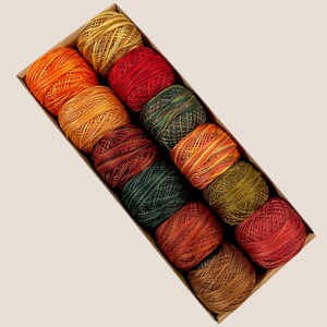 May include: A box of colorful embroidery floss in shades of orange, red, green, and gold. The spools of thread are neatly arranged in a cardboard box, perfect for crafting and embroidery projects. The threads are tightly wound.