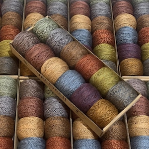 May include: A box of 10 balls of yarn in various colors, including brown, blue, green, and purple. The yarn is arranged in a circular pattern and is ready for knitting or crocheting.