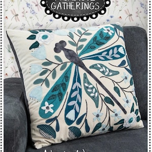 May include: A decorative pillow with a dragonfly design. The pillow features a cream-colored background with a teal and blue dragonfly and floral accents. The finished size is 22" x 22". The text "Primitive Gatherings" and "Nordic Wings" are also visible.