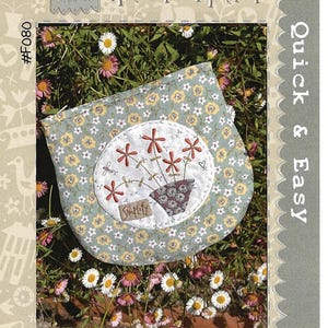 May include: A handmade pouch with a floral design. The pouch is light blue with small yellow and white flowers. A white circle features a flower pot with red flowers. Text on the pouch reads "Simplify" and "Daisy Do Pouch".