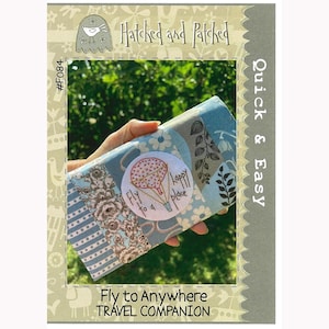 May include: A blue and white fabric travel wallet with a hot air balloon design and the text "Fly to a Happy Place". The wallet is held in a hand against a green background. The text "Hatched and Patched" and "Quick & Easy" are visible on the image. The text "Fly to Anywhere TRAVEL COMPANION" is also visible on the image.