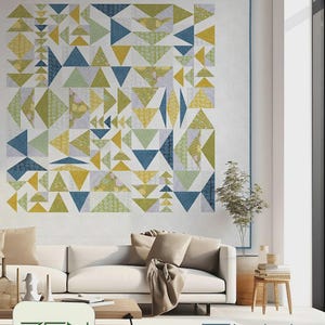 May include: A large, geometric quilt with a modern design hangs on a white wall. The quilt features triangles in shades of blue, yellow, and green. The words "ZEN CHIC" and "FLY WITH ME" are also visible.