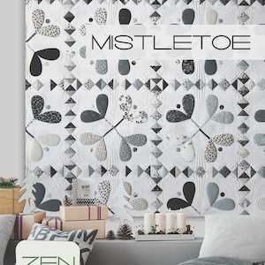 May include: A white quilt with a repeating pattern of stylized mistletoe leaves in shades of gray and black. The word "MISTLETOE" is displayed across the quilt. The quilt is part of a holiday-themed display with gifts and candles.