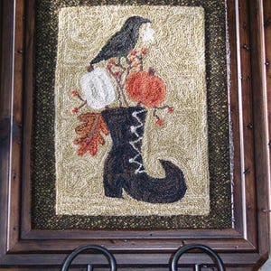 May include: A needlepoint design of a black crow perched on a branch with pumpkins and gourds in a black boot. The design is framed in a dark wood frame and the text "Something to Crow About" is below the frame.