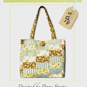 May include: A patchwork tote bag featuring a variety of floral and striped fabric patterns in shades of brown, blue, and cream. The bag has two shoulder straps and a single button closure. A tag attached to the bag reads by p.s. Penny Sturges.