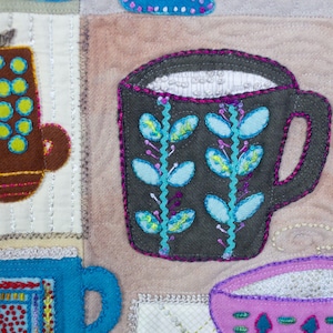 Puede incluir: Un primer plano de una obra de arte de tela colorida con una variedad de tazas y jarras. Las tazas est&aacute;n hechas de fieltro y est&aacute;n decoradas con bordados. La pieza es un mosaico de diferentes telas y colores.