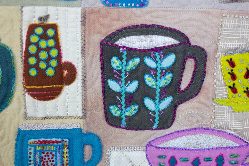 Puede incluir: Un primer plano de una obra de arte de tela colorida con una variedad de tazas y jarras. Las tazas est&aacute;n hechas de fieltro y est&aacute;n decoradas con bordados. La pieza es un mosaico de diferentes telas y colores.