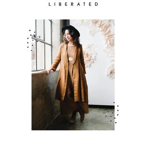 May include: A woman wearing a brown linen duster coat and dress, with a black hat and boots. The image includes the text "SEW LIBERATED" and "LICHEN DUSTER". The background features a white wall with floral decorations and a window.