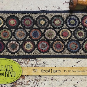 May include: An oval rug with a repeating pattern of colorful, nested circles. The rug is 4 inches by 12 inches and features a dark blue border and a neutral background. The text "Threads that Bind" and "739 - Nested Layers" are visible.