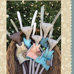 May include: A group of handmade bunny dolls in a woven basket. Each doll has a unique dress in pastel colors and a small basket. The image includes the text "Hatched and Patched" and "Bippity & Bruce (& friends)".