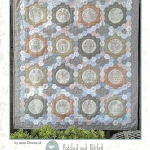 May include: A quilted textile featuring embroidered circular designs with various town-themed illustrations, set within a hexagonal pattern. The quilt is in neutral tones with accents of pink, blue, and tan. The text "AROUND TOWN" is at the top.