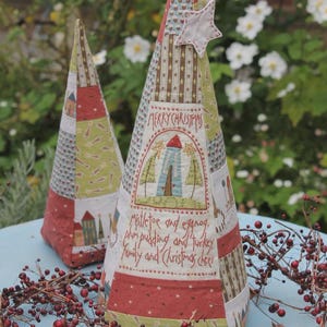 May include: Two handmade fabric Christmas tree ornaments. The larger tree is red, green, and brown with the text "Merry Christmas, mistletoe and eggnog, plum pudding and turkey, family and Christmas cheer". The smaller tree is red, green, and blue.