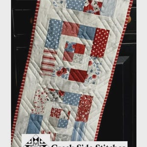 May include: A quilted table runner with a patchwork design featuring red, white, and blue fabrics. The runner measures 13 inches by 46 inches. The text "Charming You" and "Creek Side Stitches" are visible.