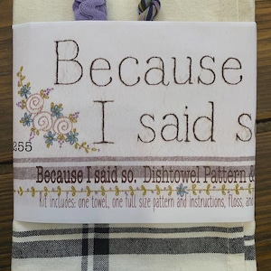 May include: A white and cream-colored dish towel kit with the text "Because I said so." The kit includes a towel, pattern, and floss. The towel has a black and white plaid pattern at the bottom and a striped pattern at the top.
